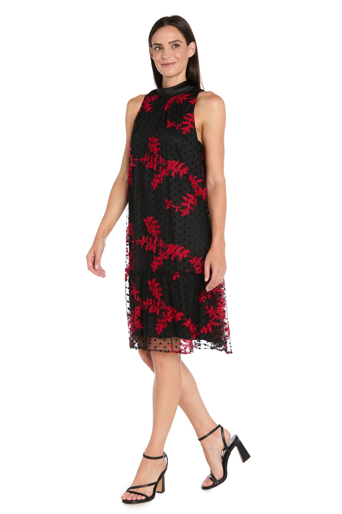 A woman models the R&M Richards 4328 Black/Red Short Party Dress with red floral patterns and black heels, standing against a white background.
